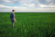 Handsome farmer. Young man walking in green field. Spring agriculture.