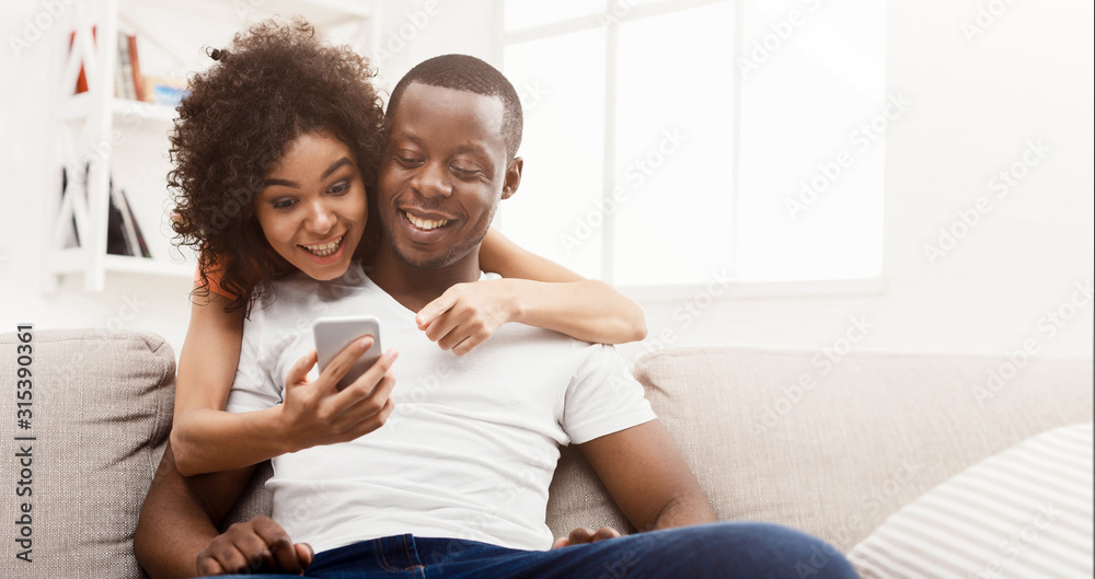 Cheerful african couple shopping online on cellphone - obrazy, fototapety, plakaty 