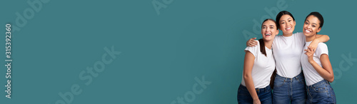 Fotografía Three Girls Embracing Smiling At Camera On Turquoise Background, Panorama