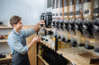 © Iryna - Sustainable shopping at small local businesses. Close-up image of man owner pours granola in paper bag from dispensers in plastic free grocery store. Seller workong in zero waste shop.