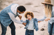 © Gabriel Trujillo/ADDICTIVE STOCK - Cheerful multiracial parents in stylish casual clothes holding smiling adorable curly ethnic toddler and having fun at sandy landscape