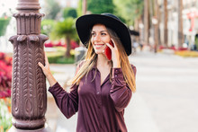 Content Long Haired Lady In Fashionable Black Hat And Shirt Walking On The Street While Calling On Mobile Phone And Looking Away At City Street