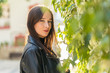 © Javier De La Torre/ADDICTIVE STOCK - Attractive tender smiling lady in leather jacket standing near green foliage of tree in daytime looking at camera