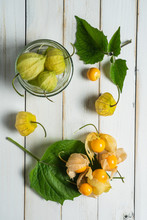 Physalis Fruit (Physalis Peruviana) Also Called Uchuva, Cape Gooseberry Or Gold Berries, Native Of Peru, On A Wooden White Board With Leaves.