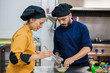 © Javier De La Torre/ADDICTIVE STOCK - Young female cook in yellow uniform holding plate and tongs and male colleague in dark blue uniform holding bowl with food while working together in kitchen and preparing delicious dish
