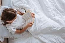 top view of girl reading book while chilling in bed
