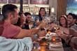 © PHILIPPE DEGROOTE/ADDICTIVE STOCK - Multiethnic friends in casual clothing gathering at festive table and making toast at stylish restaurant