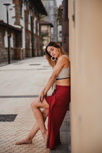 Side View Of Barefoot Woman In Trendy Top And Skirt Leaning On Building Wall And Looking At Camera While Spending Time On Street Of Old Town