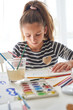 © PHILIPPE DEGROOTE/ADDICTIVE STOCK - Little girl taking watercolor with brush while sitting at table and painting at home
