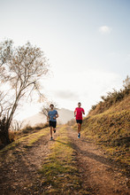 Strong Active Males In Sportswear Running Together On Dirt Road In Mountains In Sunny Autumn Day