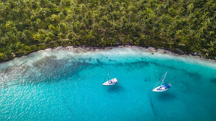 San Blas Islands, Panama - Aerial Drone Top Down View of two Sailing Yachts anchored in Turquoise Water right next to perfect White Sand Beach of Caribbean Tropical Island full of green Palm Trees.