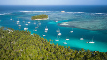 San Blas Islands, Panama - The Sailing Paradise! Aerial Drone Shot Of Many Sailboats Anchored In Blue Lagoon Next To Tropical Island With Green Palm Trees Surrounded By Coral Reefs In Caribbean Sea.