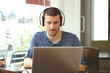 © Antonioguillem - Front view of adult man using laptop and headphones