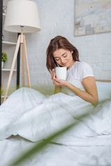 Wall Mural - selective focus of happy young woman holding cup with tea in bed