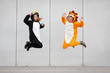 © Westend61 - Two women in penguin and lion costume jumping in front of concrete wall