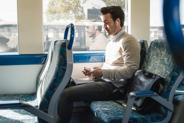 Young man with earphones using smartphone and tablet on a train