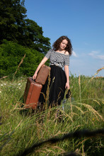 Portrait Of Young Woman On A Meadow With Many Suitcases