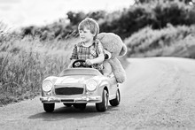 Little Preschool Kid Boy Driving Big Toy Car And Having Fun With Playing With His Plush Toy Bear, Outdoors. Child Enjoying Warm Summer Day In Nature Landscape.