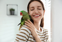 Young Woman With Cute Alexandrine Parakeet Indoors