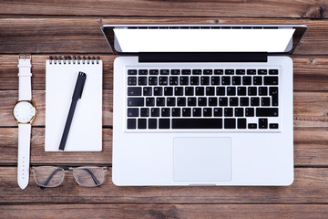 Laptop computer with glasses, notepad and wrist watch on wooden table