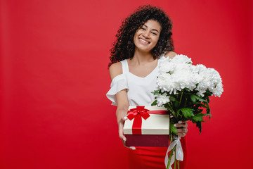 beautiful black woman smiling with gift box and bouquet of white flowers isolated over red background