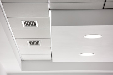 multi-level ceiling with three-dimensional protrusions and a suspended tiled ceiling with a built-in round led light and a ventilation grille.