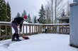 Mature woman shoveling fresh wet snow off a cedar deck railing, snow day