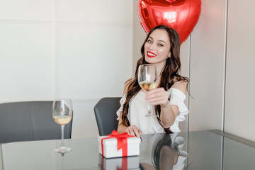 Wall Mural - cheerful young woman drinking wine from glass at home with heart shaped balloons