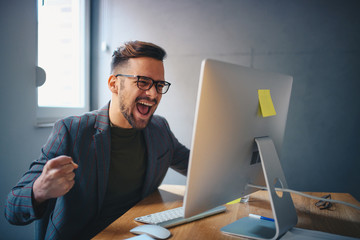 A man celebrating in front of his PC indoors.