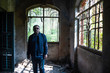 © abir - An Indian middle aged brunette man in winter clothing and sunglasses standing inside the ruins of an abandoned house with large windows. Vintage house and Indian lifestyle