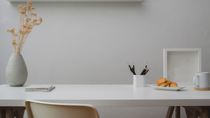 Wall Mural - Close up view of workspace with copy space, decorations, stationery, coffee cup and croissant on white table with white wall
