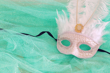 Photo of elegant and delicate white Venetian mask over mint chiffon background