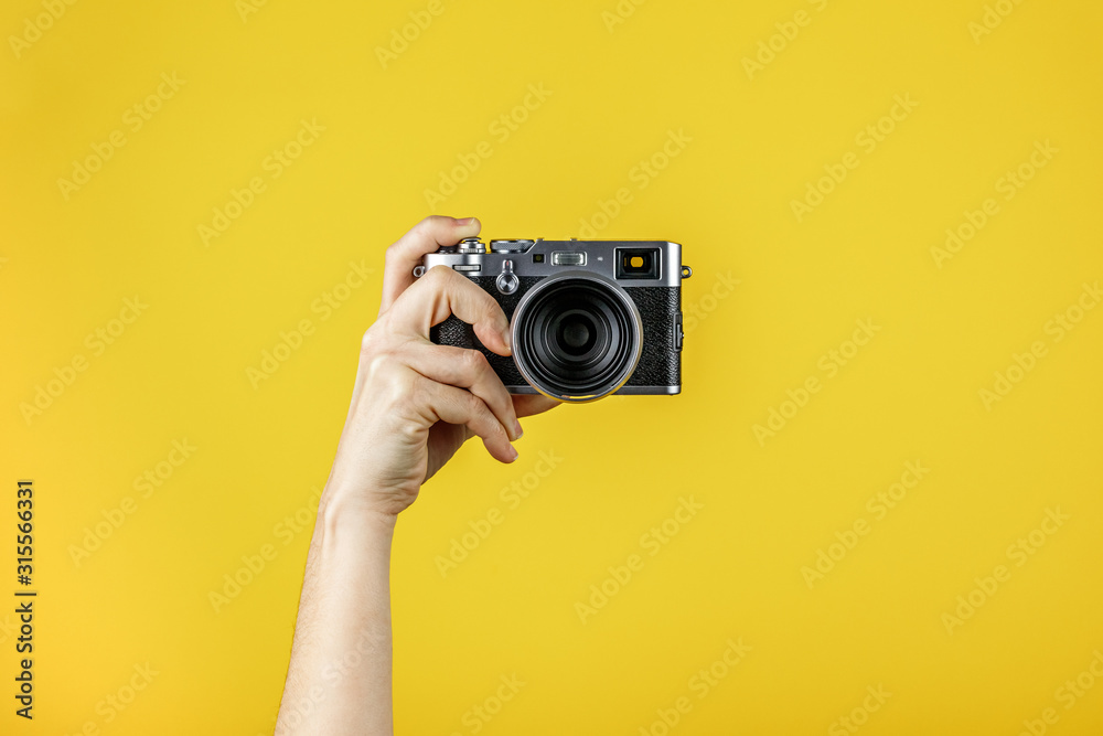 Camera held by one hand in front of a yellow background - obrazy, fototapety, plakaty 