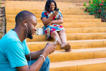 young man and woman sitting on a staircase outside using their smartphones