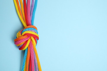 top view of colorful ropes tied together on light blue background, space for text. unity concept