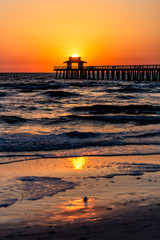 Wall Mural - Naples, Florida colorful orange sunset vertical view in gulf of Mexico with sun path reflection and Pier wooden jetty silhouette with horizon and ocean waves
