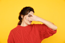 Woman Hiding Her Face And Watching Though Her Hand Isolated Over The Yellow Background