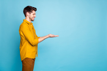 Poster - Photo of adoring man holding object with hands wearing yellow shirt trousers pants smiling toothily with eyes closed near empty space isolated over blue pastel color background