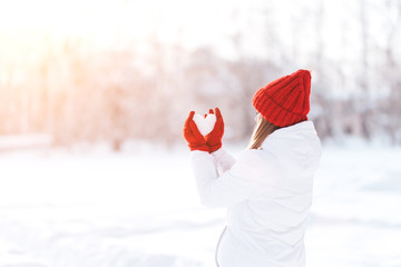 Woman in red gloves and hat holding heart shape from snow, Valentines day, sun set. love concept.