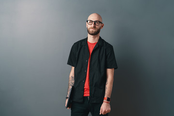 A Young bearded man with glasses holding laptop under arm in the studio on gray background