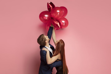 Wall Mural - happy holding balloons shaped hearts. valentine's day celebration, happy caucasian couple on coral b