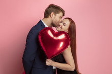 Happy Holding Balloons Shaped Hearts. Valentine's Day Celebration, Happy Caucasian Couple On Coral Background. Concept Of Human Emotions, Facial Expression, Love, Relations, Romantic Holidays.