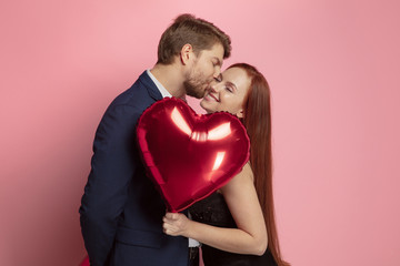 Wall Mural - happy holding balloons shaped hearts. valentine's day celebration, happy caucasian couple on coral b
