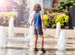 Child playing with water at street fountain in summer. Little boy playing in a fountain