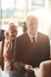 © AnnaStills - Senior businessman in suit standing near the reception and registering his ticket on business conference