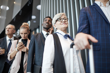 Wall Mural - Senior woman in eyeglasses standing in the queue with other people she registering before flight at the airport