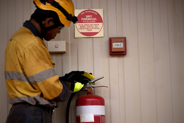 Certified safety supervisor wearing safety glove yellow fall protection helmet long sleeve shirt inspecting fire extinguisher tag ensure it's up to date testing pressure prior used construction site 