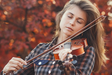 beautiful young woman playing violin on a background of red foliage, romantic girl in dress playing a musical instrument in nature, musical performance outdoors, concept of hobby and passion in art