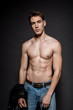 © LIGHTFIELD STUDIOS - sexy young man with muscular torso in jeans holding biker jacket on black background
