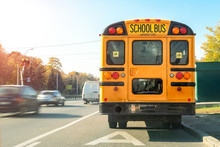 Big Classic Vintage American Yellow Schoolbus Standing On A Bus Lane At Highway And Waiting Pupils And Children For School Trip Road. School Bus Transport Back Door View On Route Bright Morning Time